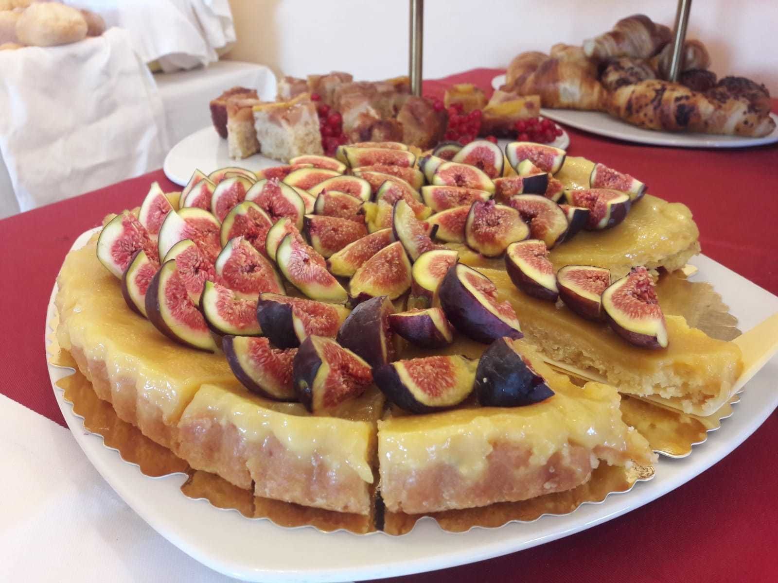 A round tart topped with sliced figs and a golden crust, surrounded by other pastries on a table.