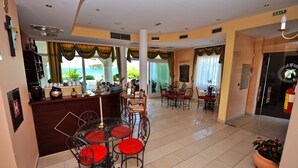 A hotel lobby with a reception desk, multiple dining tables with red chairs, and a view of the ocean through large windows. - Villa Kastel (Povljana)