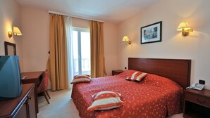 A hotel room with a large bed, two bedside lamps, a desk with a television, a chair, and a window with curtains. - Villa Kastel (Povljana)