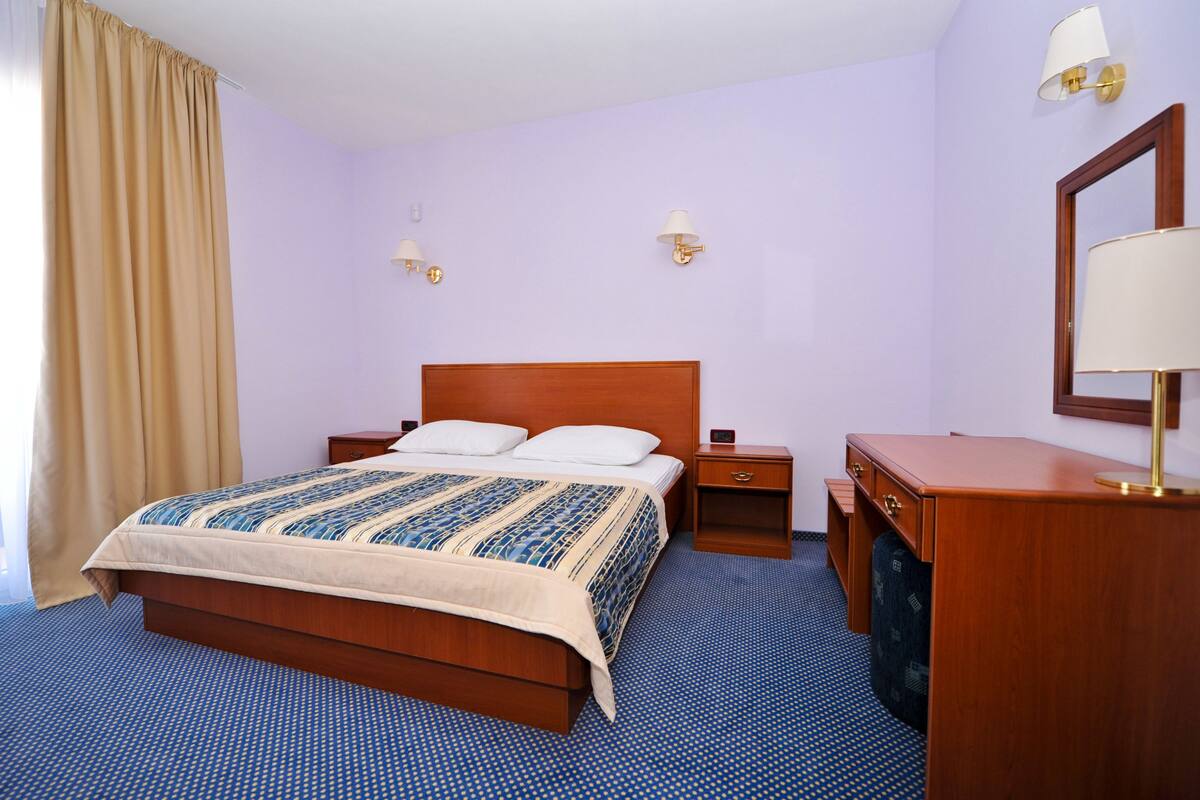 A hotel room with a wooden bed, two bedside tables, a desk, and a mirror.