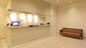 A reception area with a tiled counter, a laptop, a phone, and a couch. - Reco Hotel Mikuni (Toyonaka)