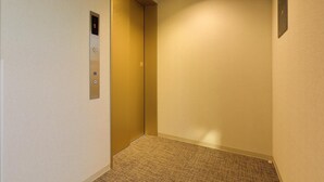 A narrow hallway with a carpeted floor, a wall-mounted elevator control panel, and a plain wall. - Reco Hotel Mikuni (Toyonaka)