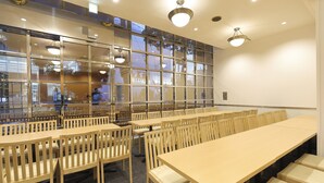 A conference room with multiple tables and chairs, large windows with reflections, and ceiling lights. - Reco Hotel Mikuni (Toyonaka)
