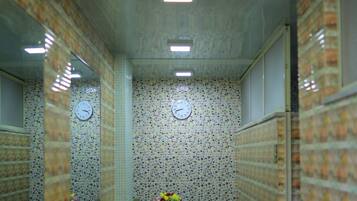 Un pasillo estrecho con paredes de azulejos, un reloj y una pequeña mesa con un arreglo floral.