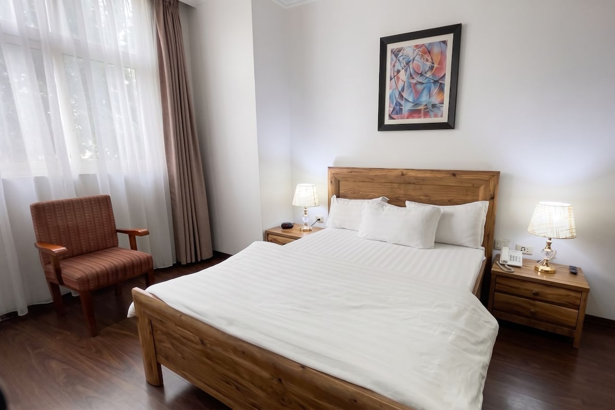 Une chambre d’hôtel avec un grand lit, deux tables de chevet, une chaise et un tableau au mur.