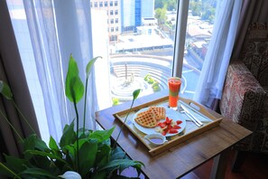 A breakfast tray with waffles, strawberries, and a drink on a table by a window with a view of a cityscape.