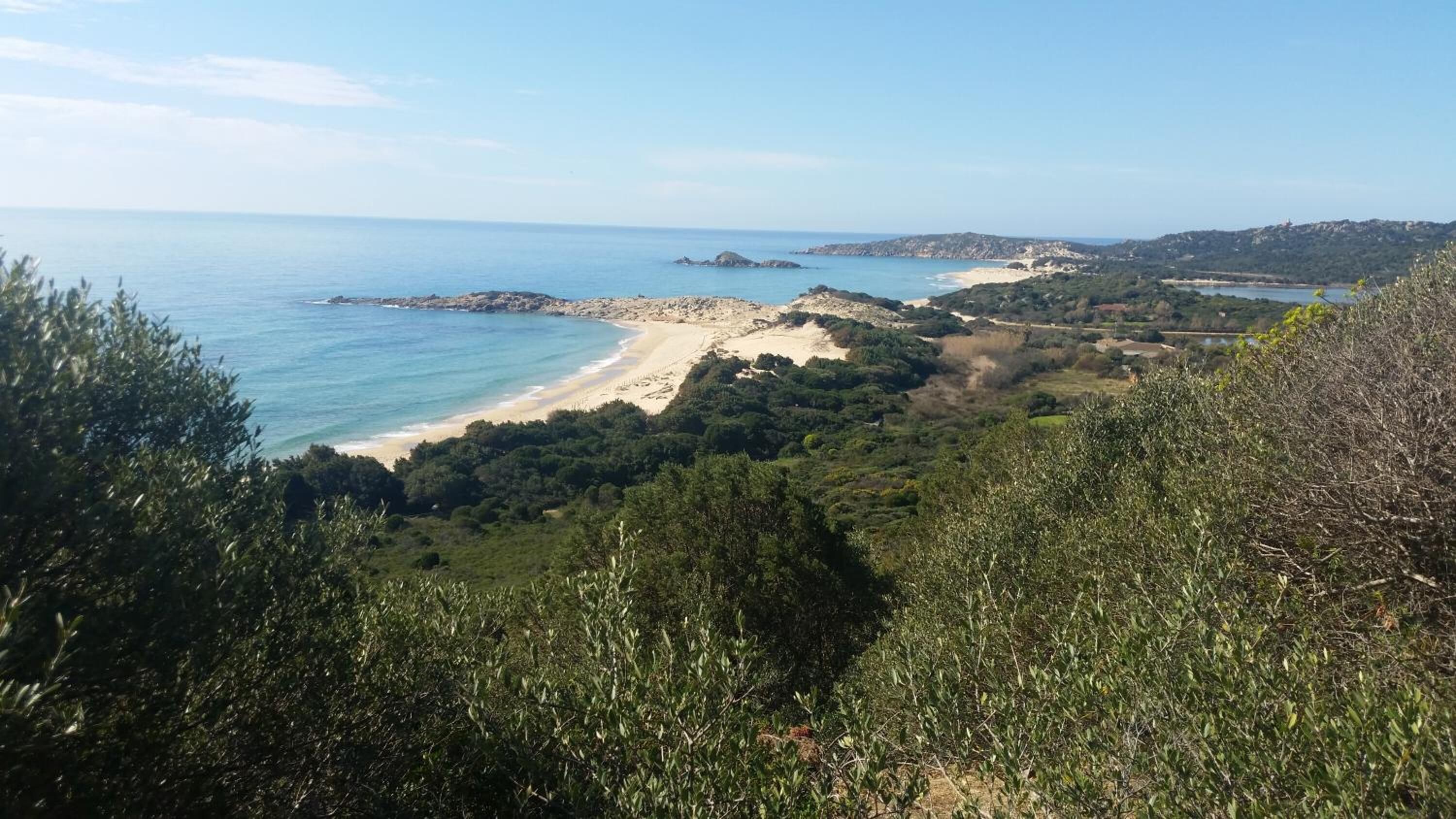 A coastal landscape with a beach, rocky outcrops, and dense greenery.