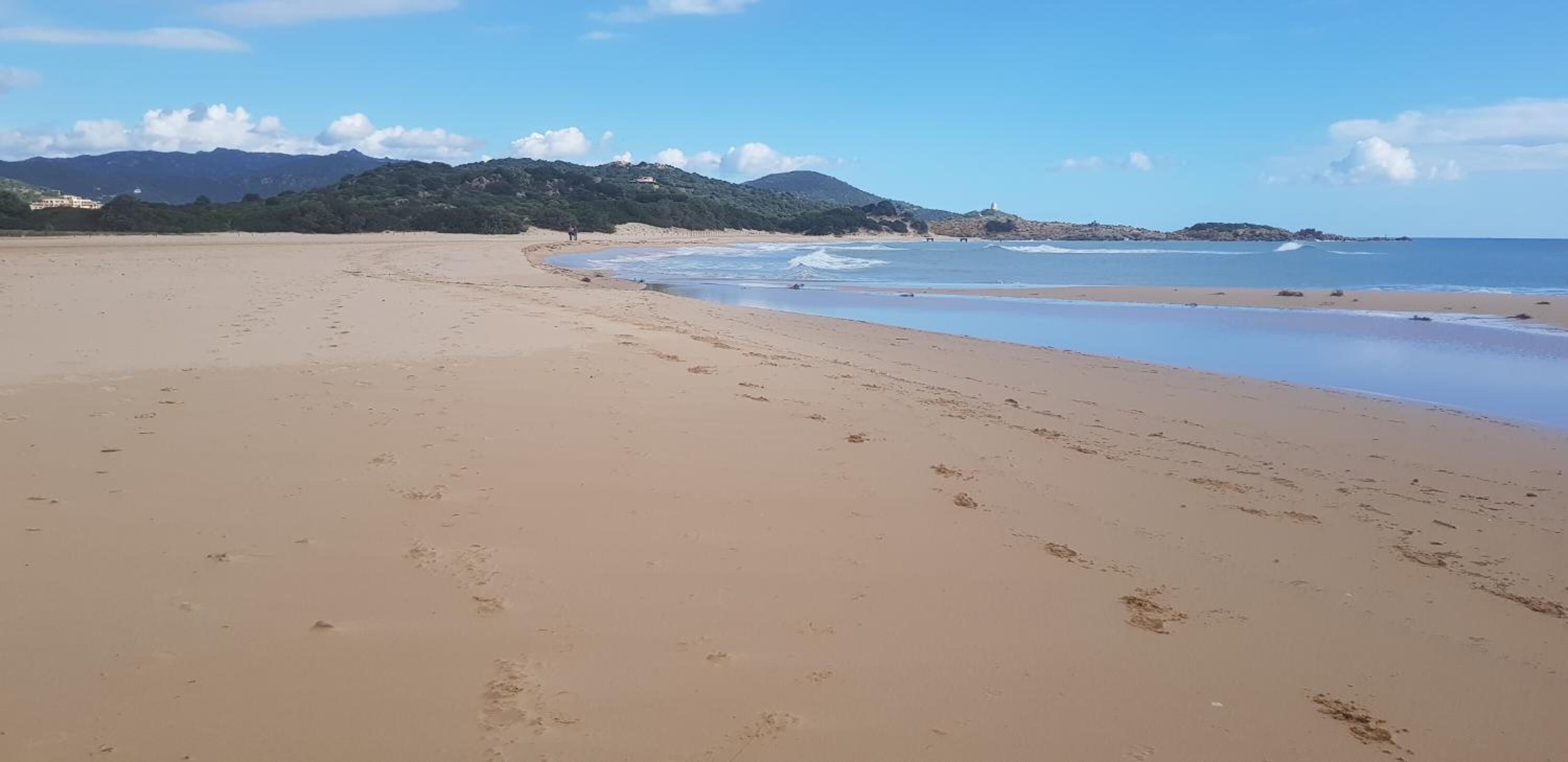 A wide sandy beach with gentle waves, a clear sky, and distant mountains.