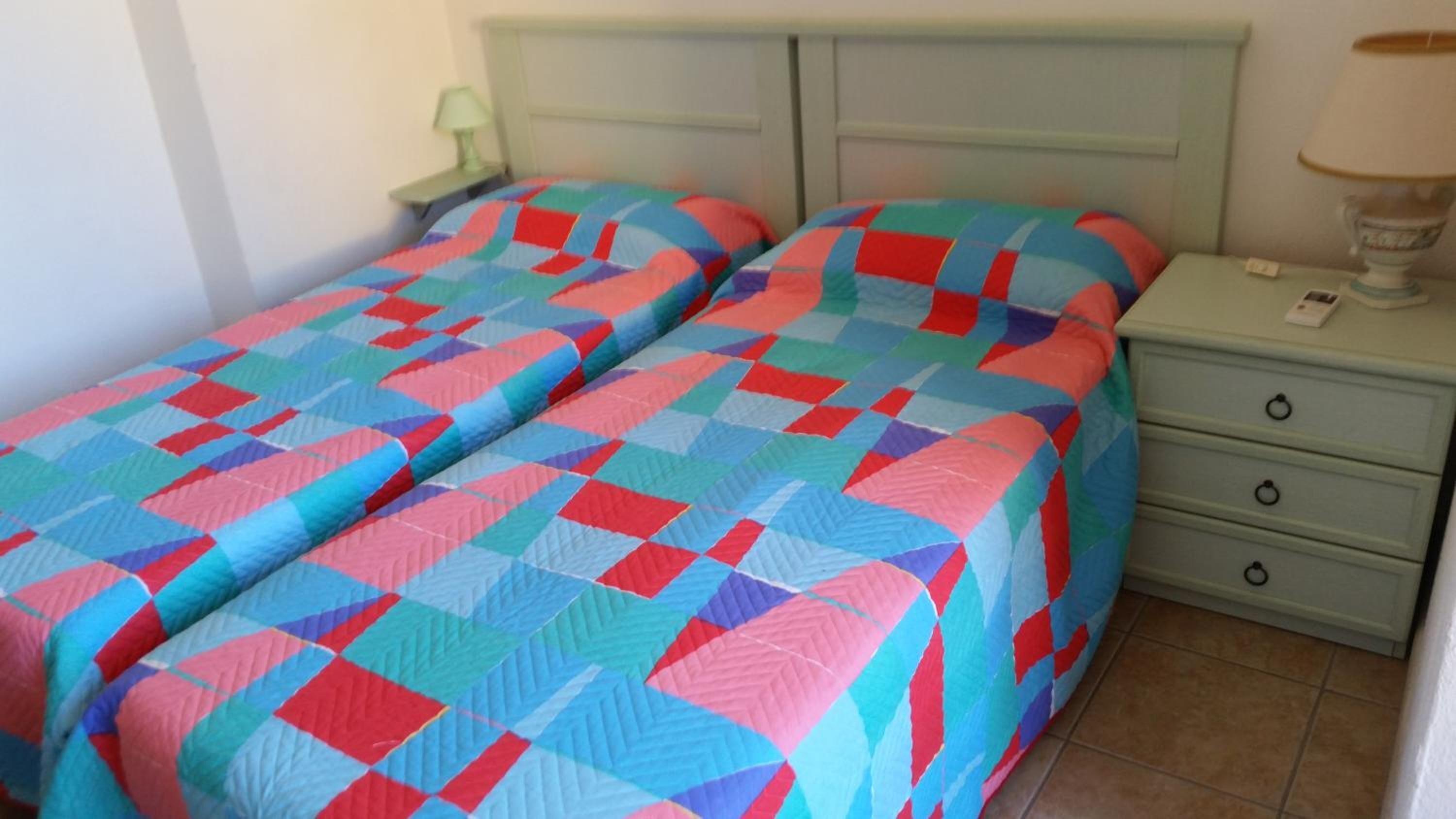 Un letto matrimoniale con una coperta colorata, un comodino con una lampada e una piccola cassettiera.