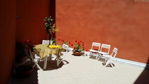 A patio with a round table, white chairs, potted plants, and red flowers. - L'Onda Blu (Domus de Maria)