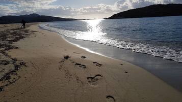 Una playa con huellas, una persona caminando y montañas al fondo.