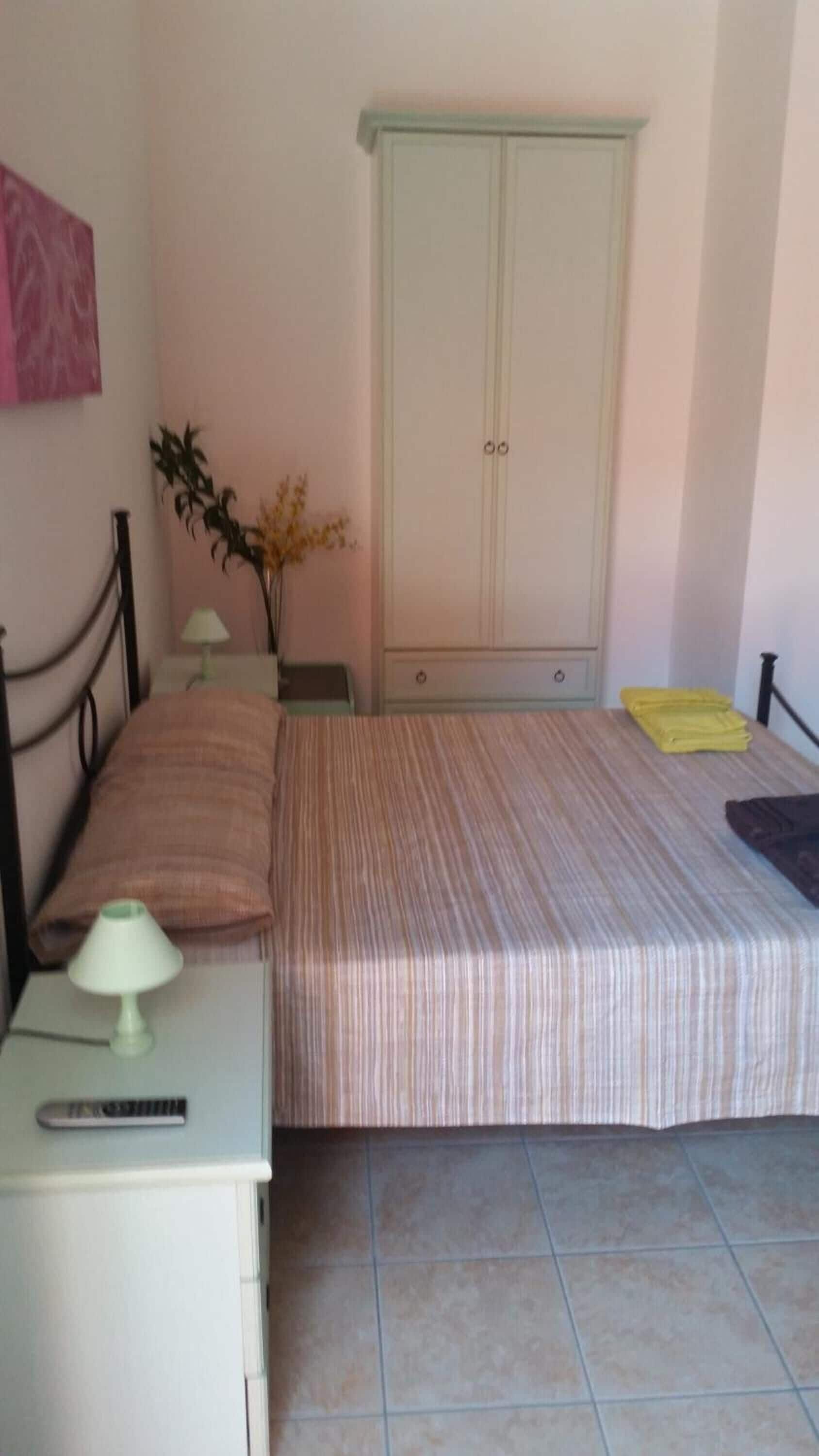 Un dormitorio con una cama, una mesita de noche, una lámpara, un armario y una planta pequeña.