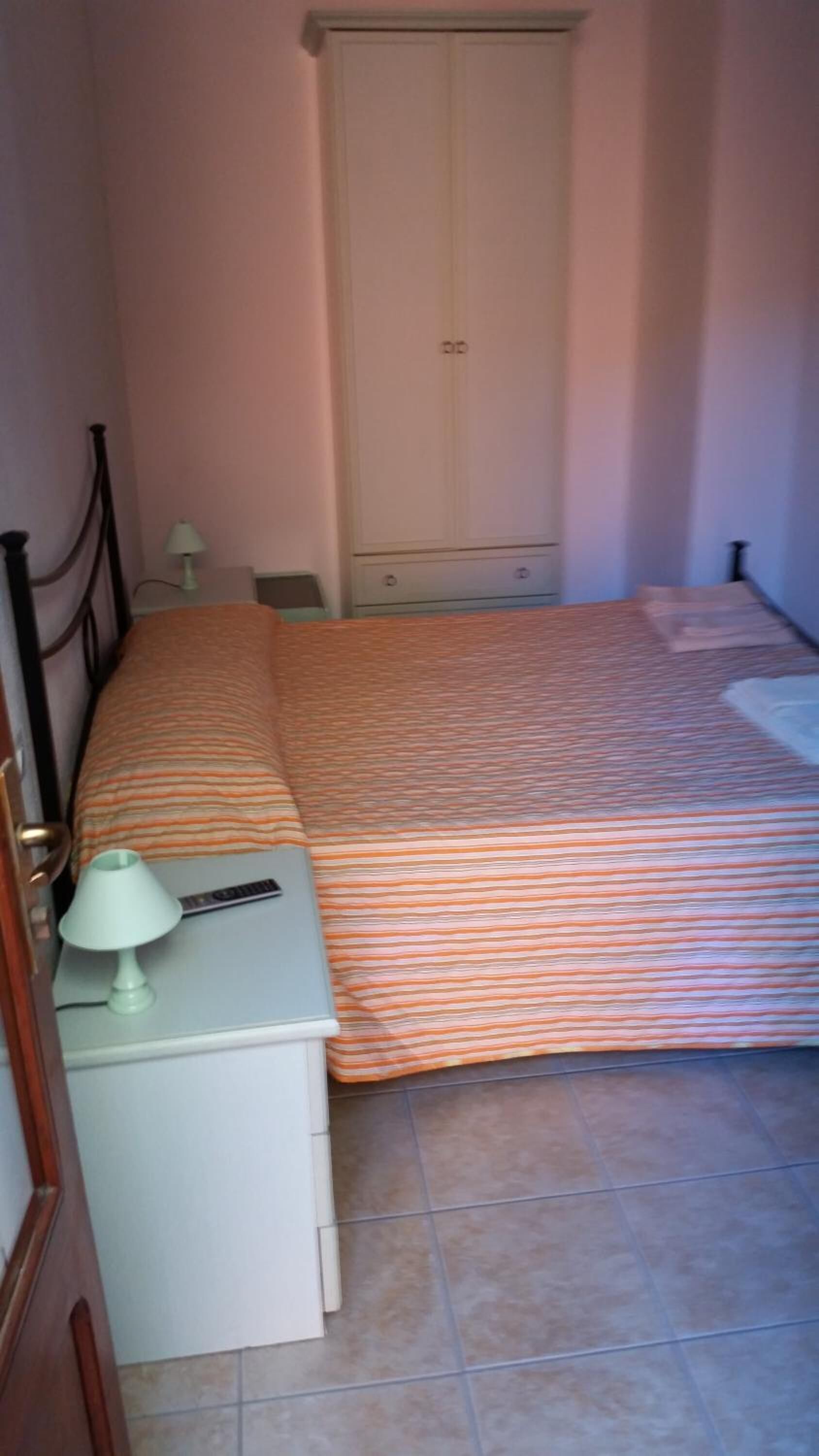 Un dormitorio con cama, mesita de noche, lámpara, armario y una pequeña mesa.
