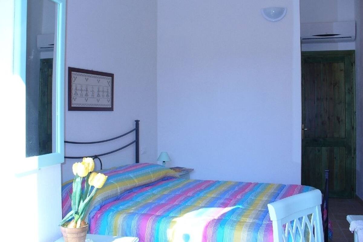 Ett sovrum med en säng, ett sängbord, en lampa, ett fönster, en spegel och en dörr.