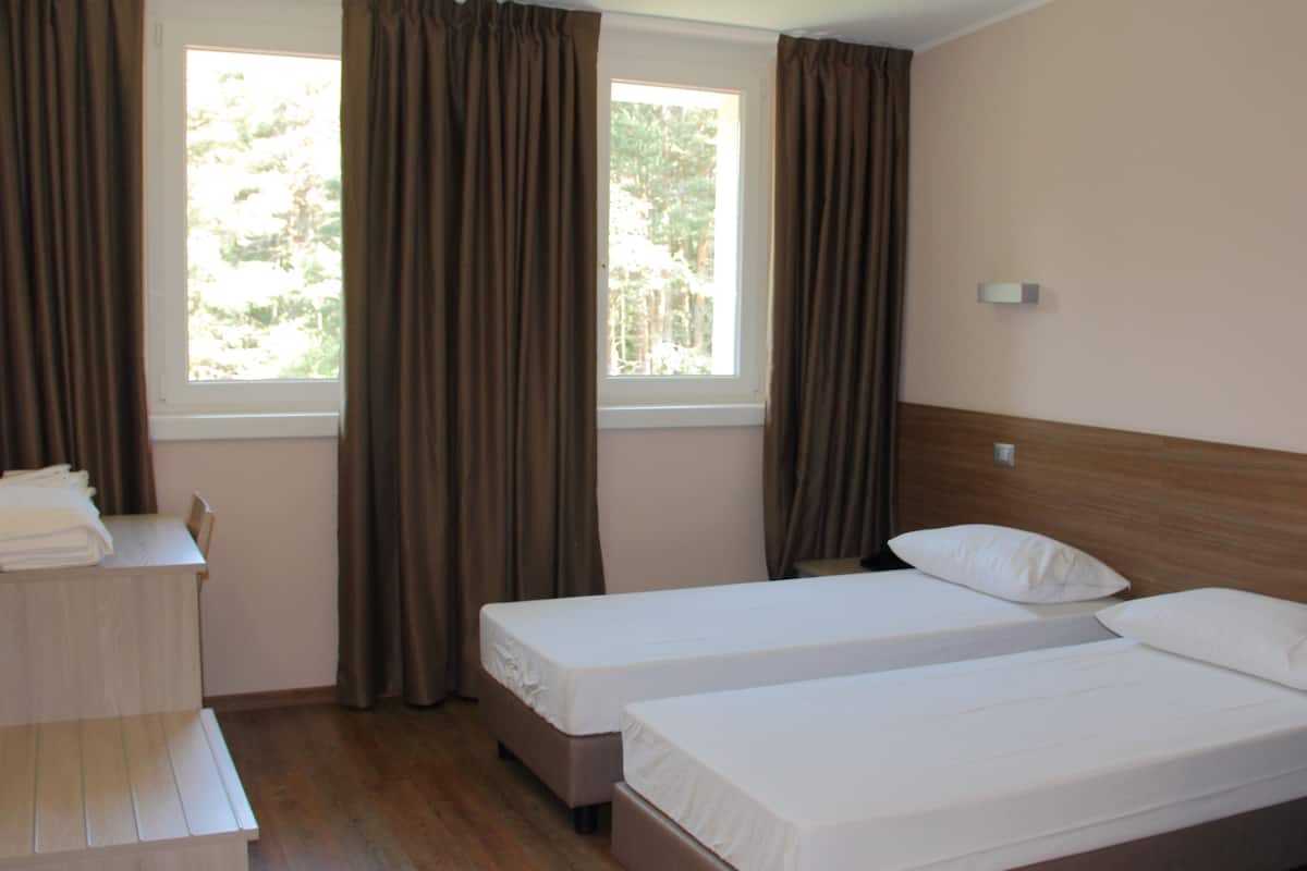 A hotel room with two single beds, a wooden desk, and a window with curtains.