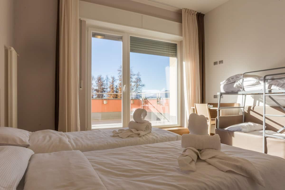 A hotel room with two beds, a window with curtains, and a view of trees and buildings outside.