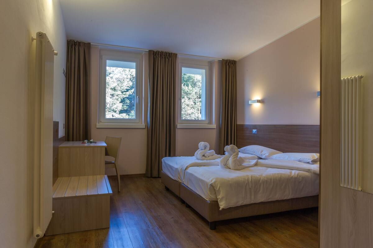 A hotel room with a bed, a desk, and two windows with curtains.