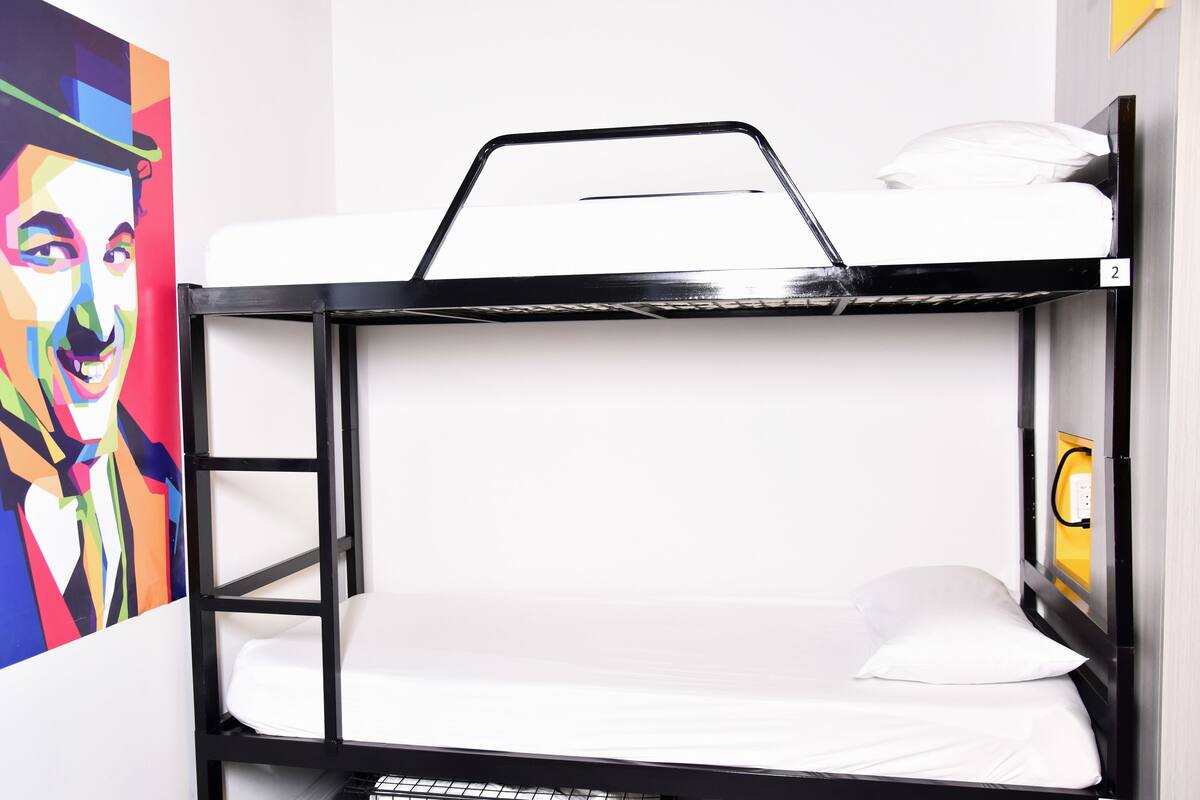 A bunk bed with a white mattress and black frame, a white pillow, and a small shelf.