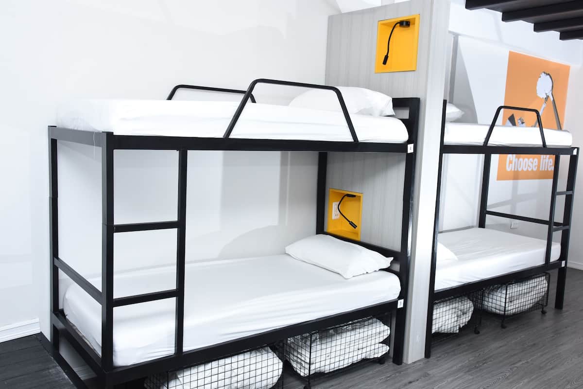 Two bunk beds with white bedding and black frames, a yellow wall-mounted shelf, and a poster with the text "Choose life."