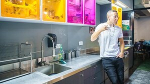 A modern kitchen with stainless steel appliances, a sink, and a window with yellow and pink lighting. - Cinema Hostel Jerusalem (Jerusalem)