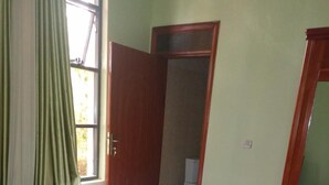 A bedroom with a bed, a wooden wardrobe, a grey rug, and a window with curtains. - Shami Luxury Apart (Kigali)