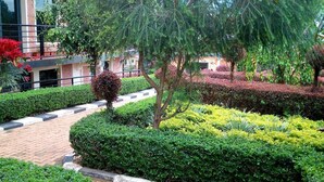 A landscaped garden with neatly trimmed hedges, a brick pathway, and a variety of trees. - Shami Luxury Apart (Kigali)