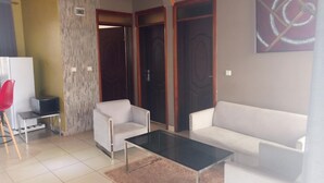 A modern living room with a white sofa, a glass coffee table, and a red chair. There is a white cabinet and a television on a stand. - Shami Luxury Apart (Kigali)