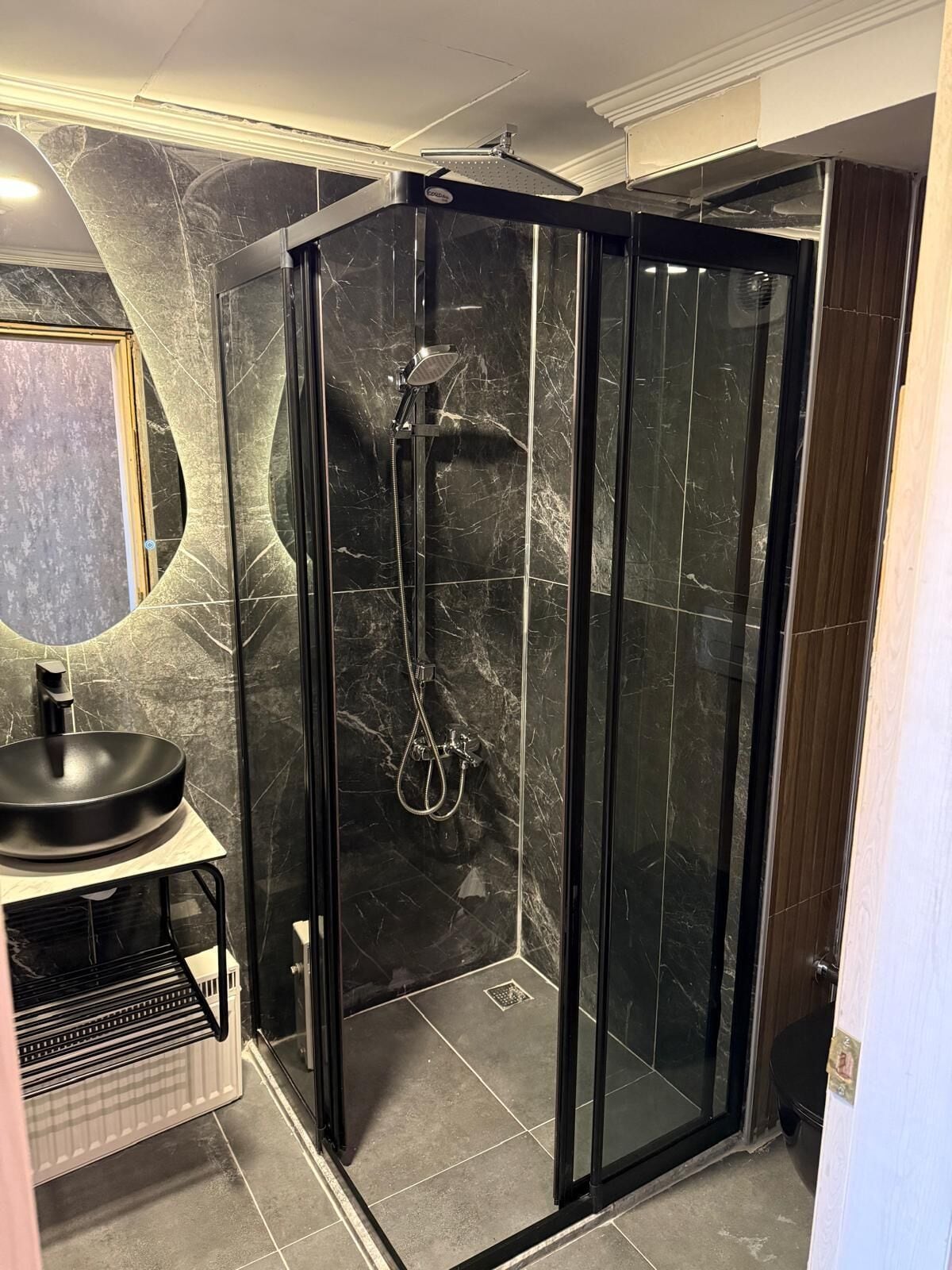 Ein modernes Badezimmer mit einer Duschkabine, einem schwarzen Waschbecken und einer Marmorwand.