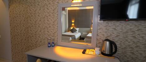 A hotel room with a desk, a chair, a mirror, a television, a bed, and a coffee maker.