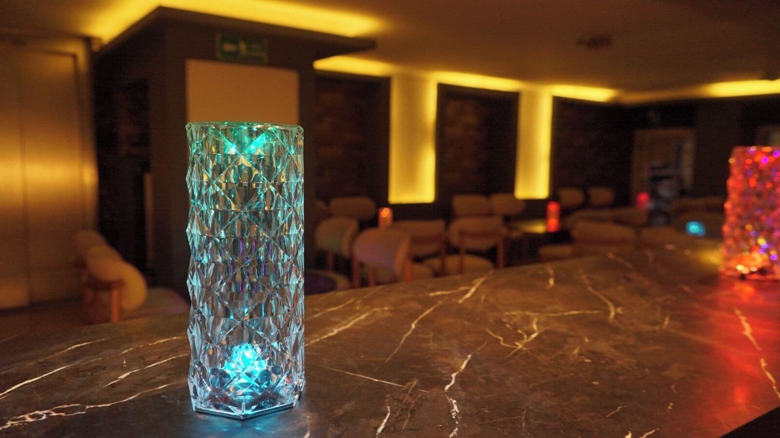 A bar area with a marble countertop, a decorative glass vase, and a seating area in the background.