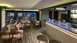 A modern bar area with seating, a counter with illuminated blue glassware, and a view of a cityscape through large windows. - Artan Hotel (Isparta)