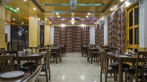 A restaurant with wooden tables and chairs, a patterned wall, and a chandelier. - Mountain View Resort (Kandaghat)