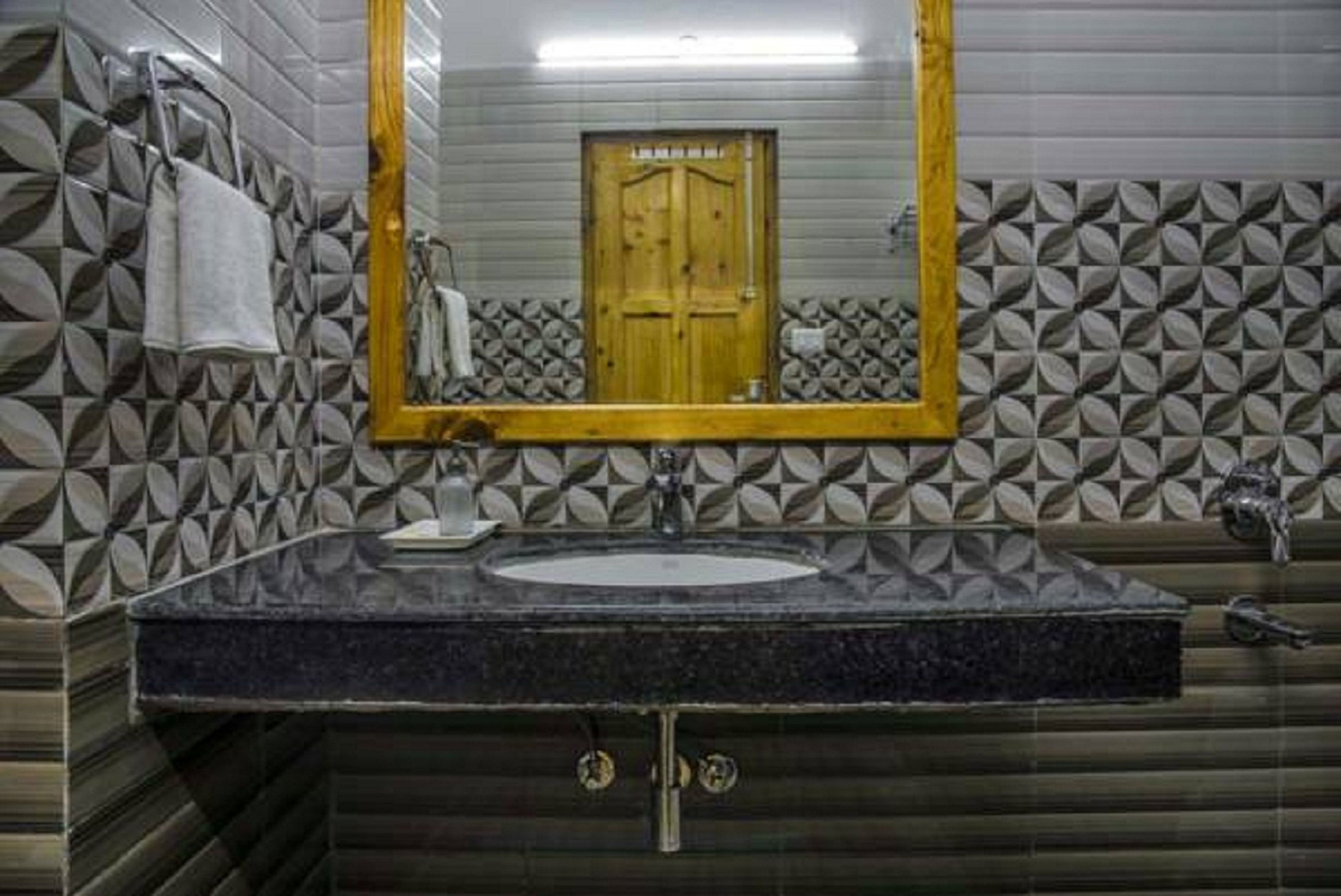 A bathroom with a black granite sink, a gold-framed mirror, and patterned tile walls.