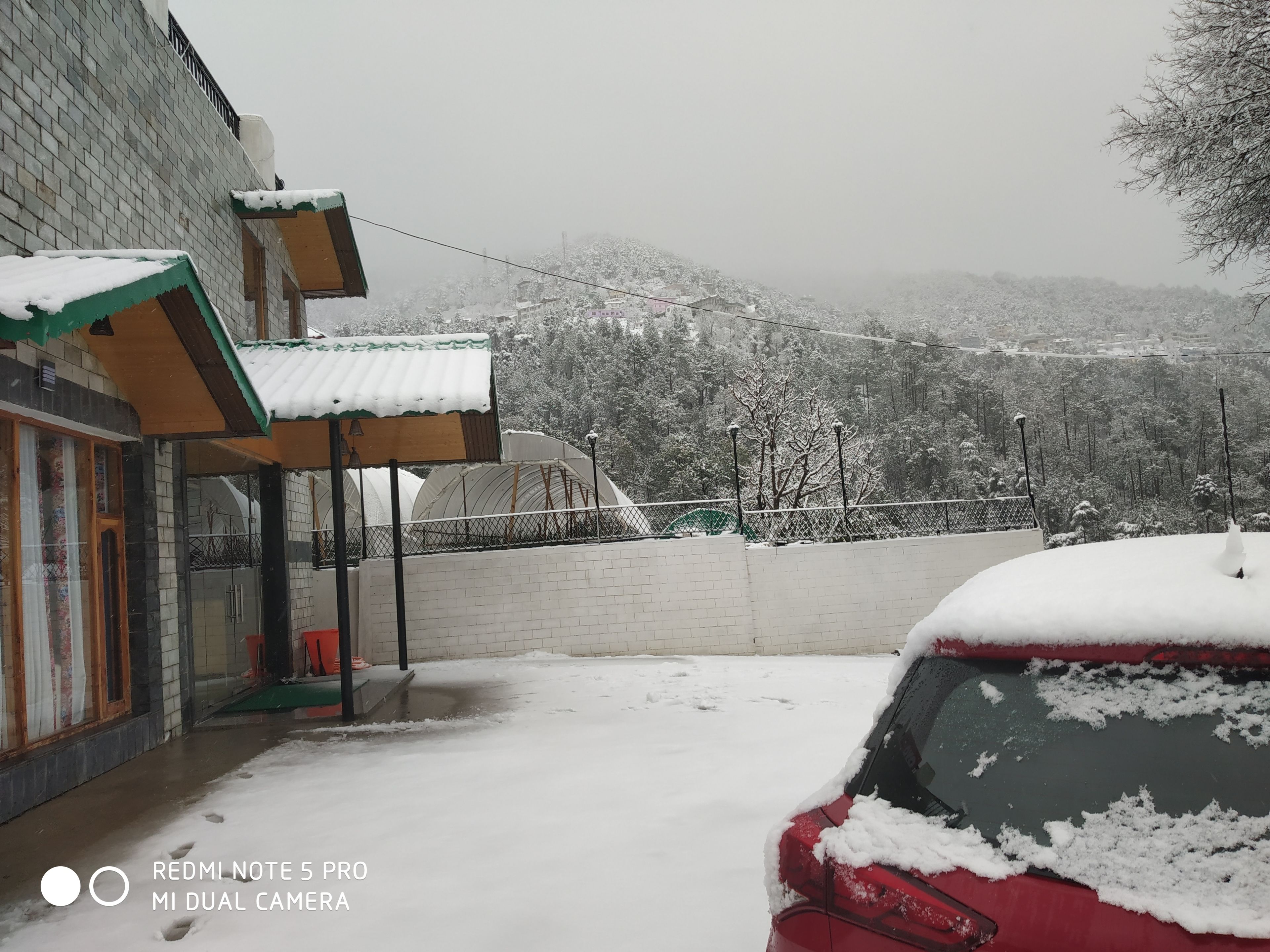 Un bâtiment doté d’une entrée abritée et d’une voiture recouverte de neige, garée devant.