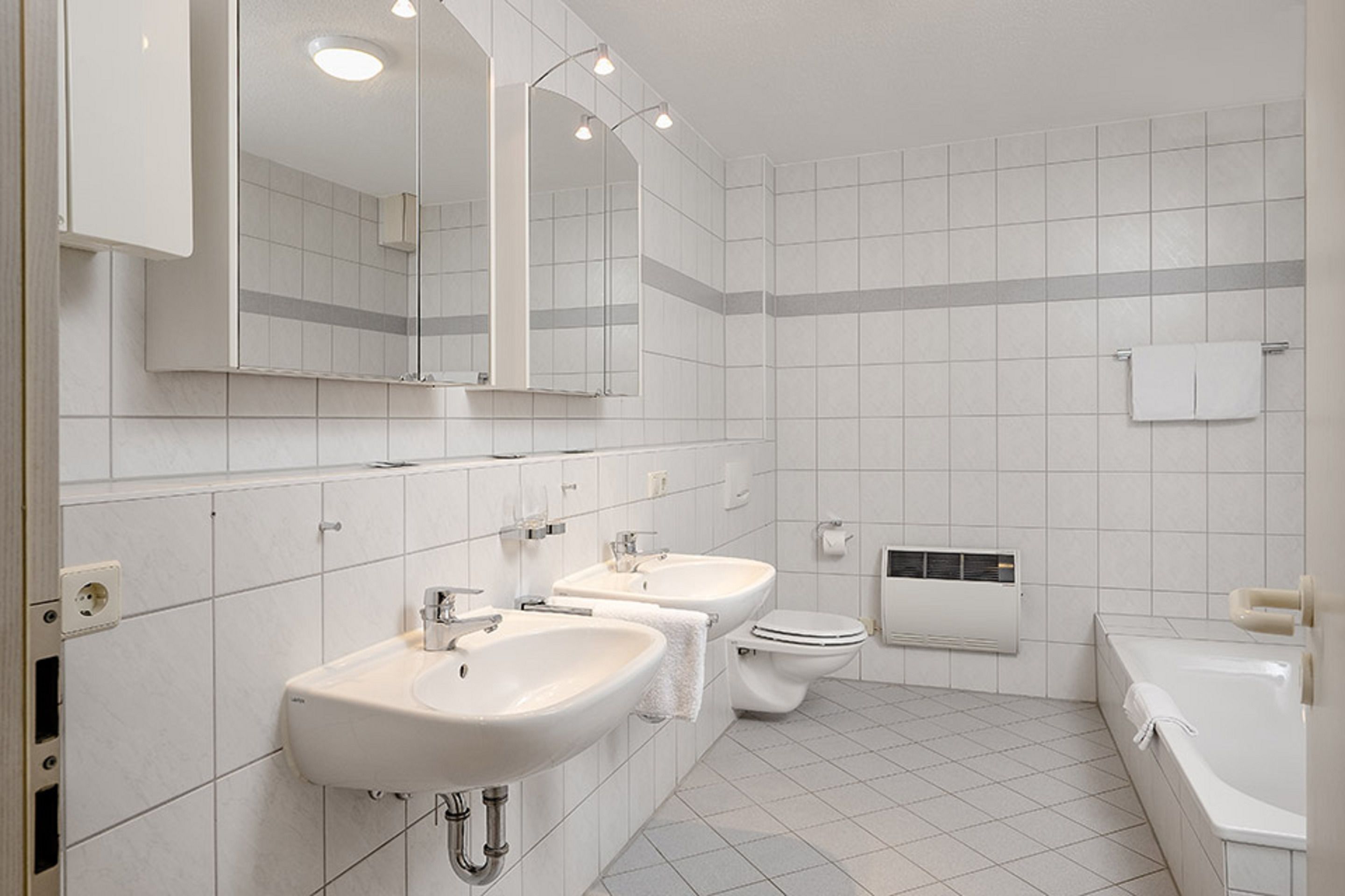Un baño moderno con dos lavamanos, un inodoro y una bañera.