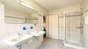 Une salle de bain avec deux lavabos, un miroir et une douche fermée par une paroi de verre.