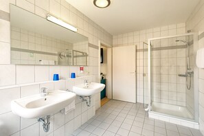 A bathroom with two sinks, a mirror, and a glass-enclosed shower. - Gästehaus Mythos (Rust)