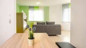 A modern living room with a grey sofa, a wooden table with a vase of flowers, and a green accent wall. - Gästehaus Mythos (Rust)