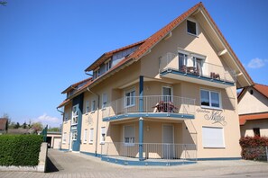 A two-story building with a balcony on the upper floor, a sign reading "Gastehaus Nittos," and a paved entrance area. - Gästehaus Mythos (Rust)