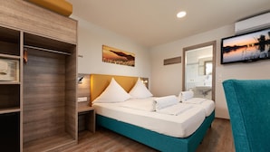 A hotel room with a bed, a wardrobe, a mirror, and a TV. - Gästehaus Mythos (Rust)