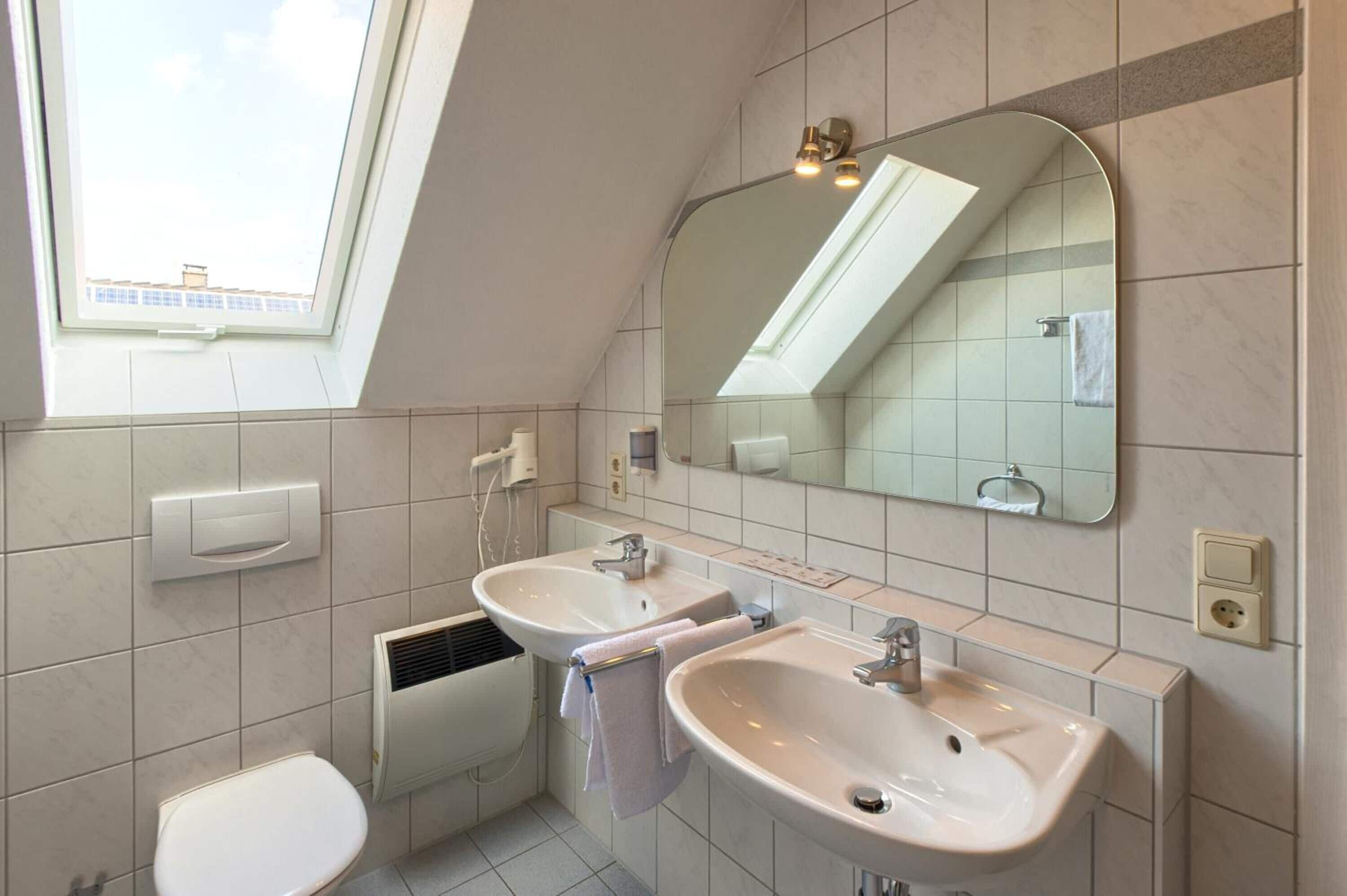 Un baño moderno con dos lavamanos, inodoro, ventana y espejo.