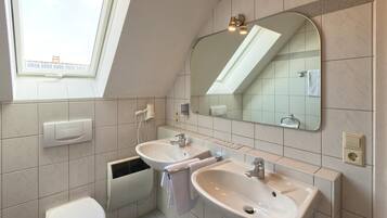Un baño moderno con dos lavamanos, inodoro, ventana y espejo.