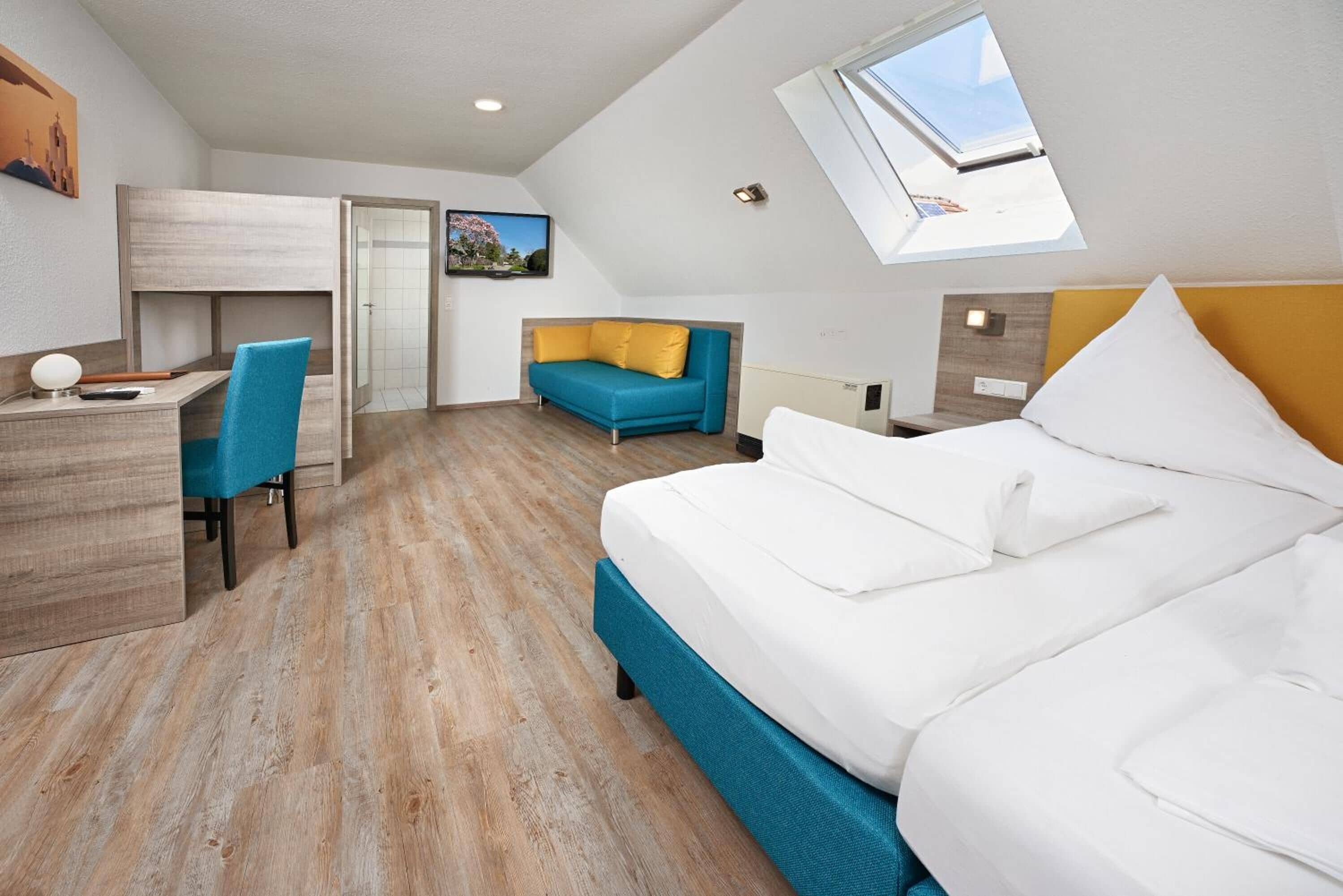 A modern hotel room with a bed, a desk, a chair, and a sofa.