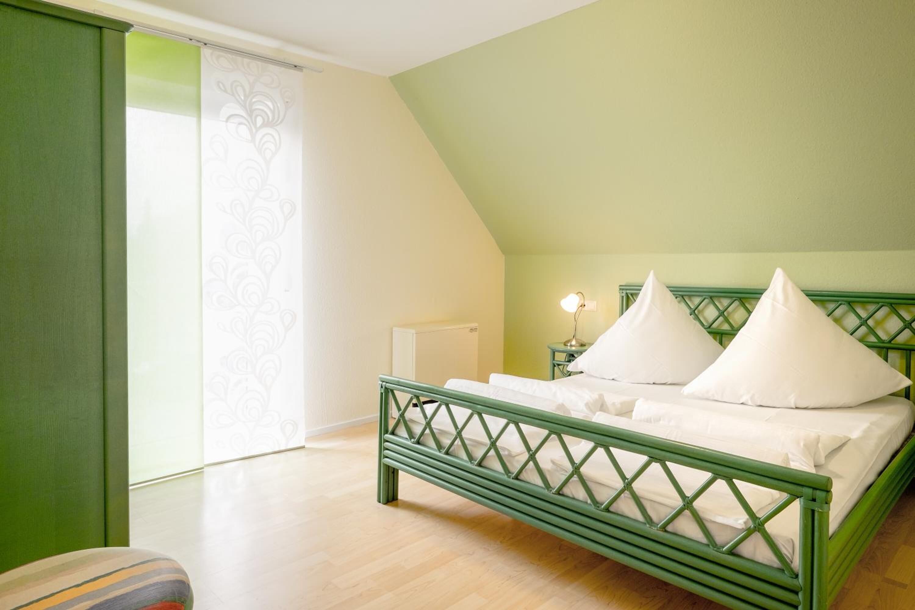 Een slaapkamer met een groen metalen bed en witte beddengoed, plus een nachtkastje met een lamp.