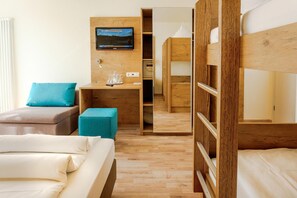 A hotel room with a wooden bunk bed, a single bed, a desk with a TV, and a small seating area.
