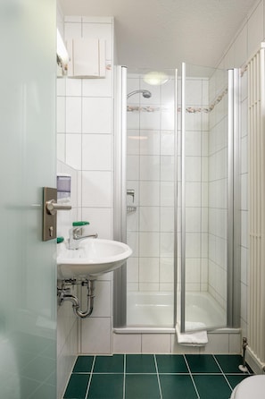 Ein Badezimmer mit einer Duschkabine, einem weißen Waschbecken mit grünem Seifenspender und einer weißen Toilette.