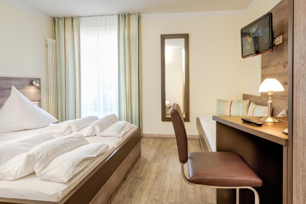 Une chambre d’hôtel avec un lit, un bureau, une chaise, une télévision et un miroir.