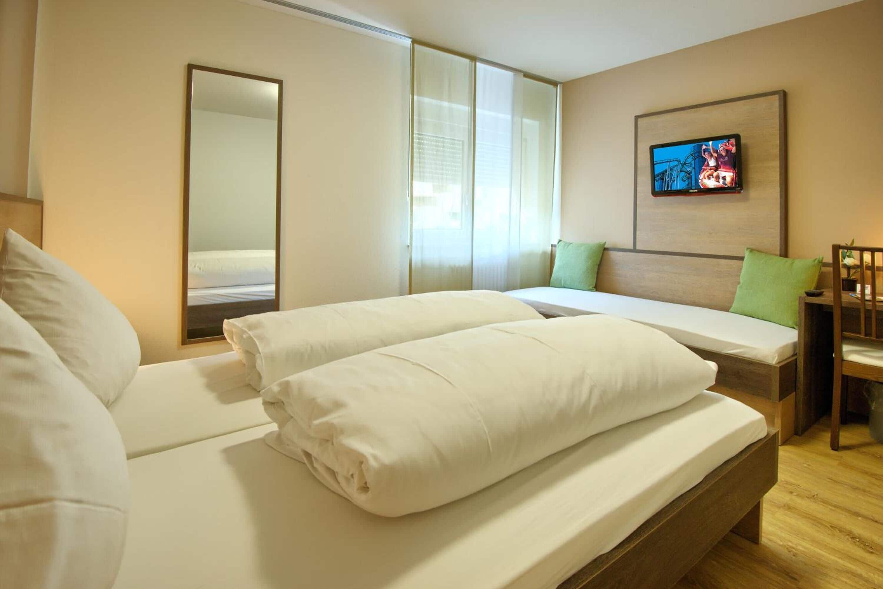 A hotel room with a bed, a TV, and a window with curtains.