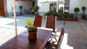 An outdoor seating area with wooden tables and chairs, potted plants, and umbrellas with Coca-Cola branding. - Hédi Vendégház (Eger)