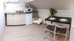 A compact kitchen with a microwave, kettle, and small refrigerator. There is a dining table with two chairs and a potted plant. - Hédi Vendégház (Eger)